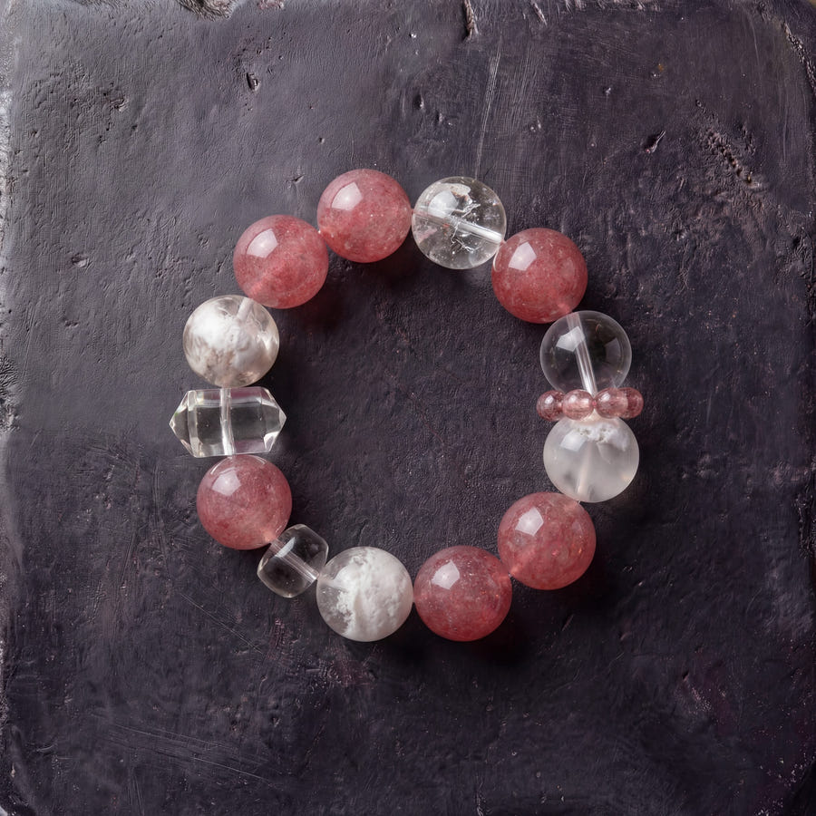 Z05 Rouge Kinetic bracelet — strawberry quartz and white phantom quartz beads, flat lay on dark stone