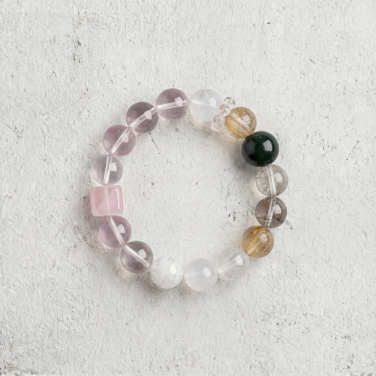 Z07 Rose Protocol bracelet top-down on light gray — rose quartz cube among pale beads